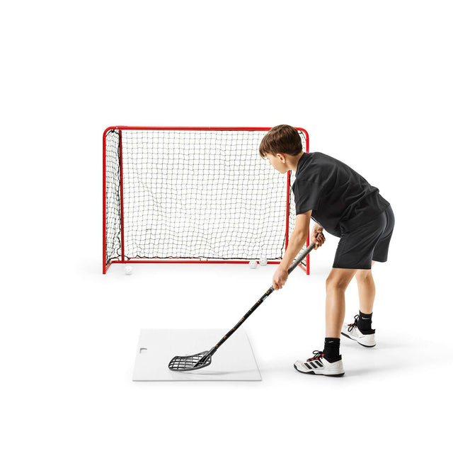 Ung kille tränar skott med skottramp innebandy och målbur för bättre skottprecision hemma.